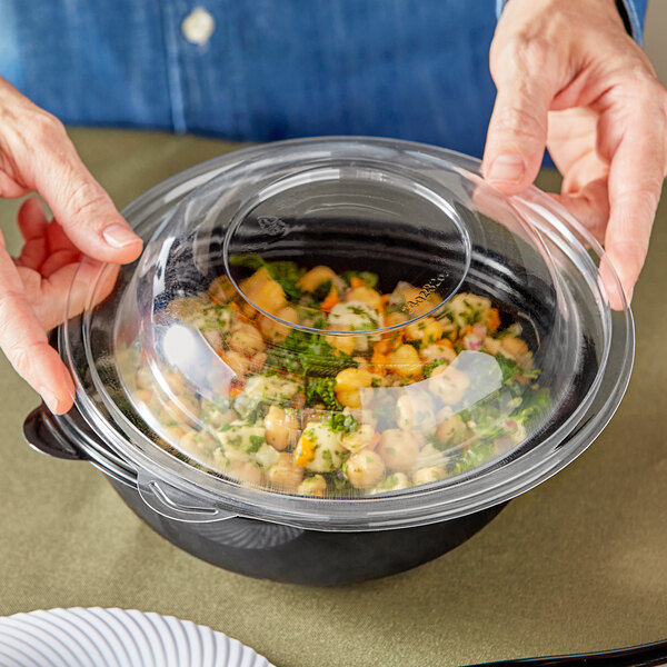 A person holding a clear container with a Visions plastic lid over a bowl of food.