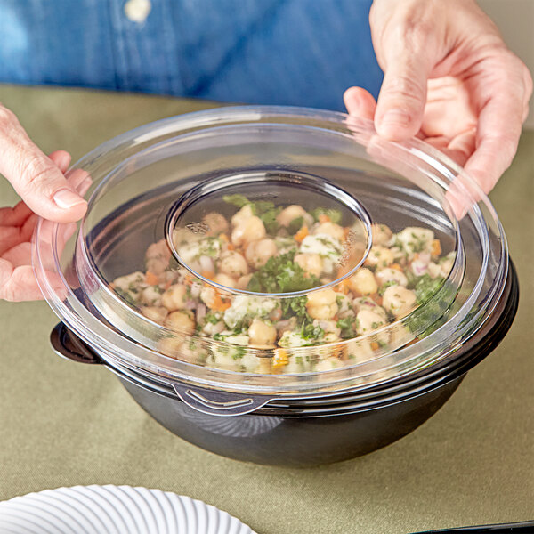 A person holding a clear bowl of food with a clear plastic lid.