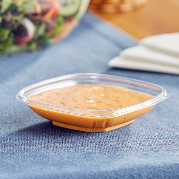 A clear plastic Visions catering bowl filled with food on a table.