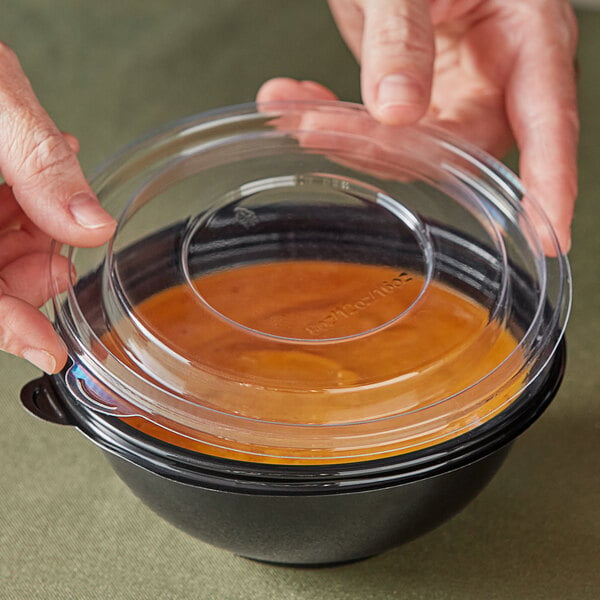 A person holding a Visions clear plastic lid over a bowl of soup.