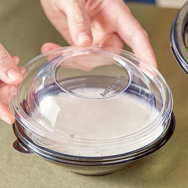 A person holding a clear plastic container with a Visions clear plastic dome lid.