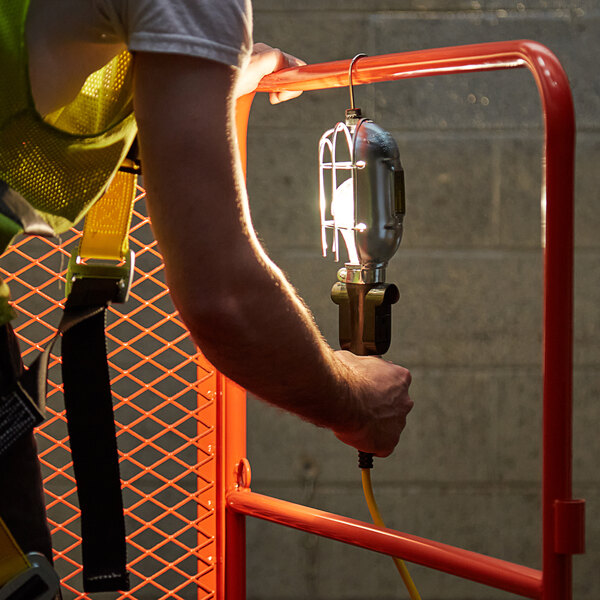 A man in a safety vest using a Voltec incandescent trouble light with a metal shade and hanging hook.
