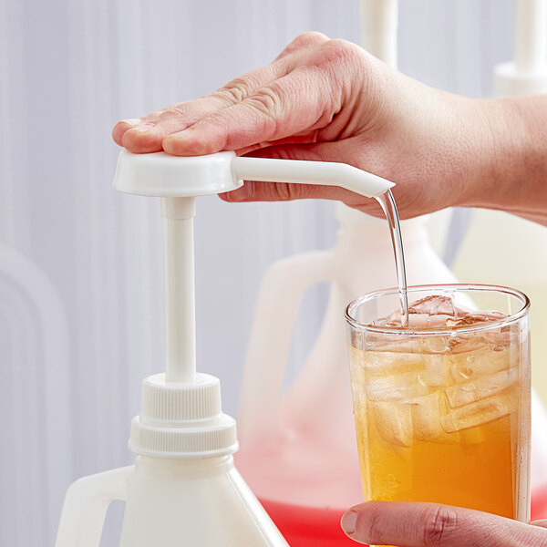 A hand using a white Tablecraft condiment pump to pour orange liquid into a glass with ice.