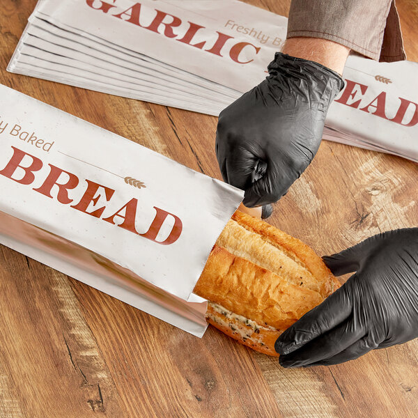 A person in black gloves putting a loaf of garlic bread in a printed foil bag.