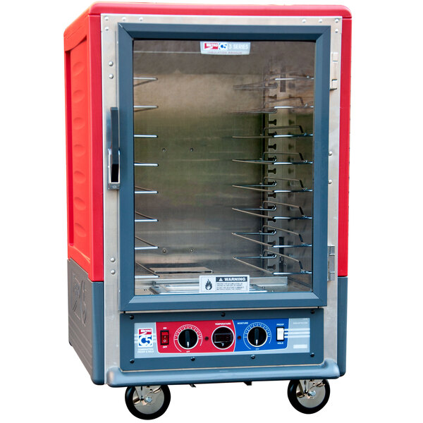 A red and grey Metro C5 heated holding and proofing cabinet with a clear door and wheels.