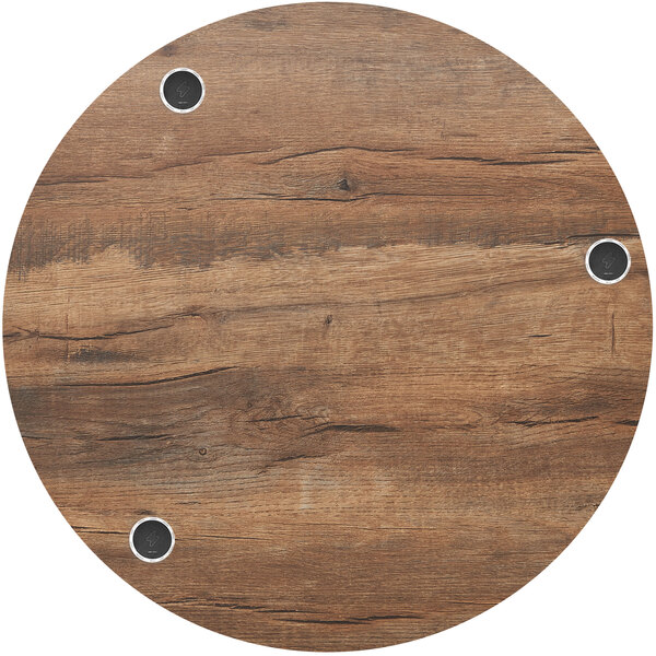 A BFM Seating round knotty pine table top with wireless chargers and holes in it.