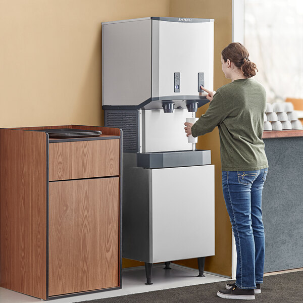 A woman using a Scotsman Meridian ice and water dispenser to fill a cup.