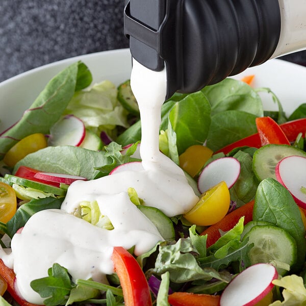 A salad with white dressing being poured into it.