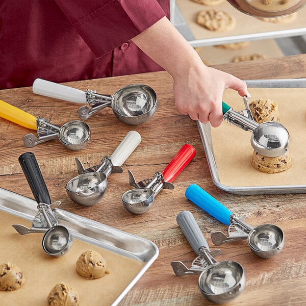 A person using a metal Choice scooper with a white handle to scoop a cookie.