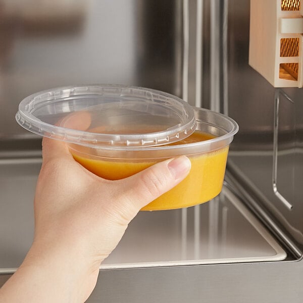 A hand holding a Choice plastic deli container with a yellow liquid in it.