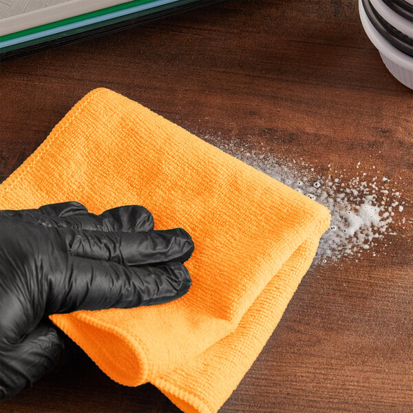 A person in black gloves cleaning a surface with a yellow Lavex Microfiber cloth.