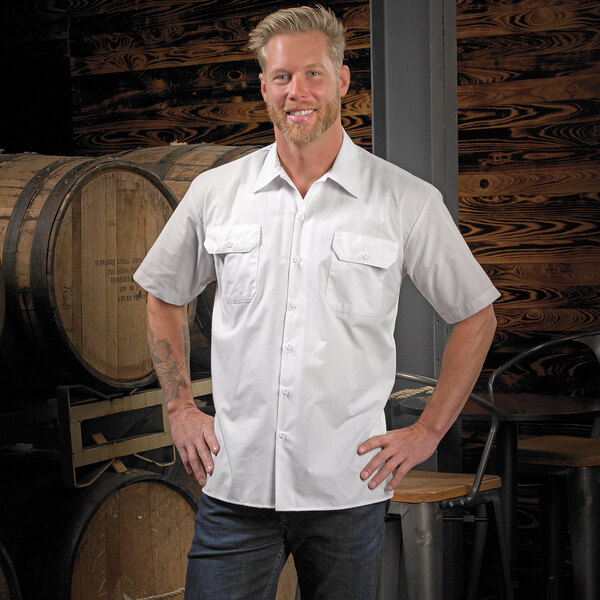 A man in a Mercer Culinary white short sleeve work shirt standing in front of barrels.