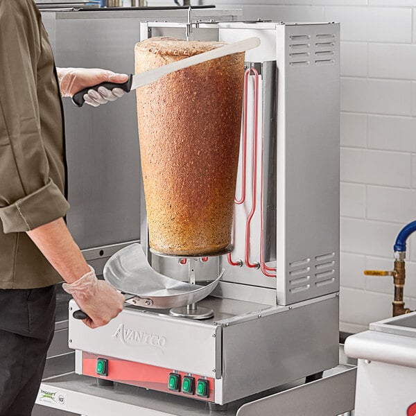 A man using an Avantco Electric Vertical Broiler to cut gyro meat.