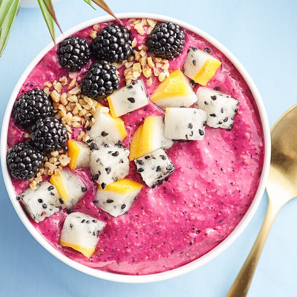 A bowl of pink Pitaya Foods smoothie with blackberries and pineapple.
