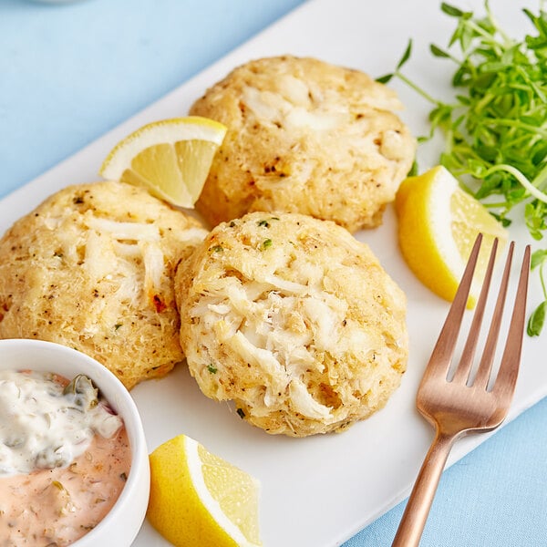 A white plate with three Handy Ultimate Crab Cakes with lemon slices.