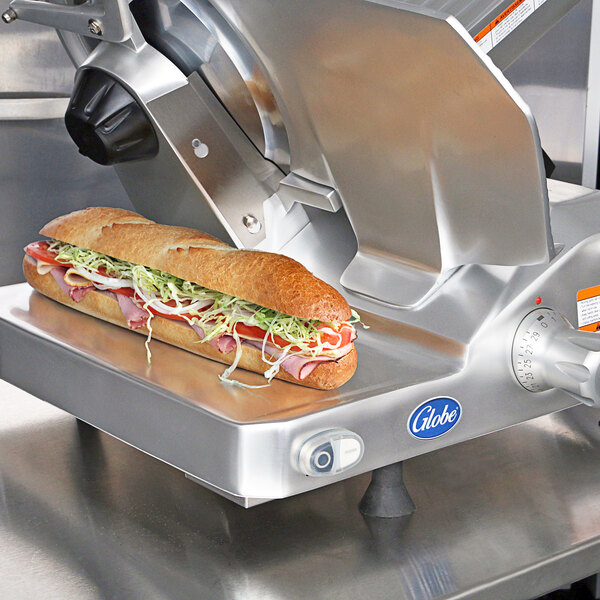 A sub sandwich being sliced on a Globe medium duty meat slicer.