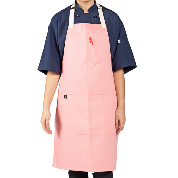 A woman wearing a coral pink Uncommon Chef bib apron with natural webbing.