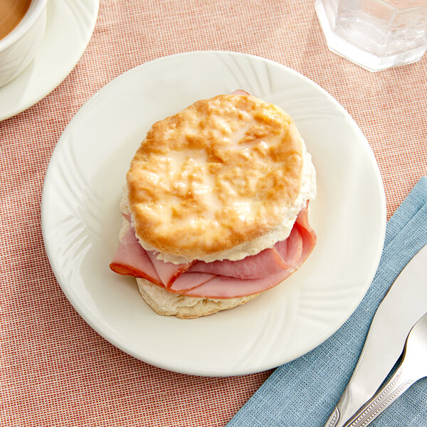 An Acopa ivory stoneware plate with a ham and cheese biscuit sandwich.