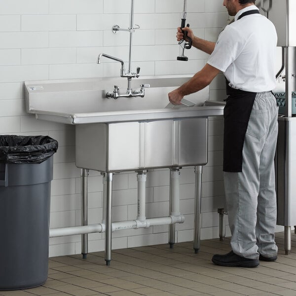 A man wearing an apron standing next to a Steelton 3 compartment sink.