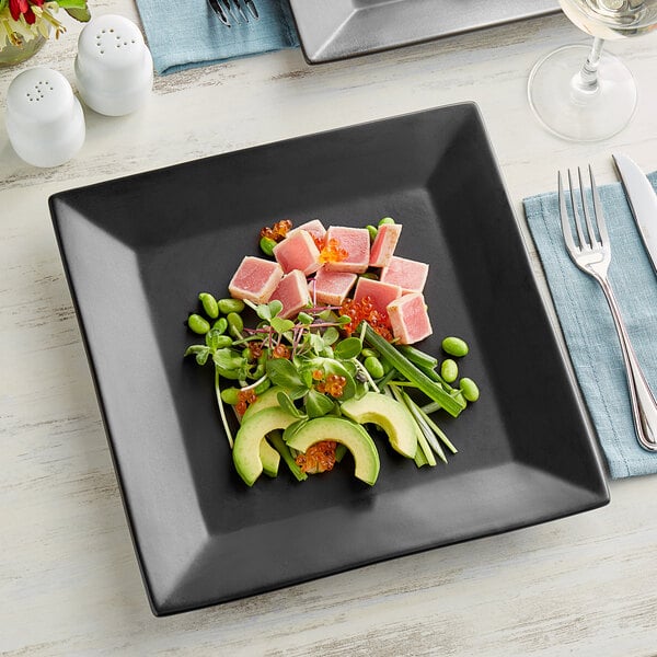 An Acopa matte black square stoneware plate with food on a table.