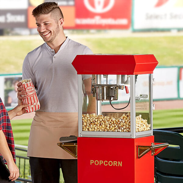 A man standing next to a Carnival King popcorn machine holding a bag of popcorn.