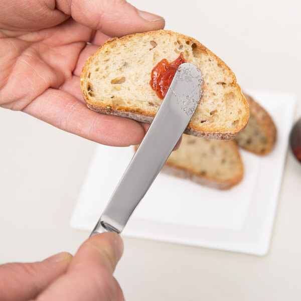A person using a Vollrath Queen Anne stainless steel butter knife to spread jam on a piece of bread.