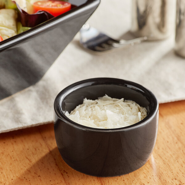 A close-up of a glossy black stoneware ramekin filled with shredded white food.