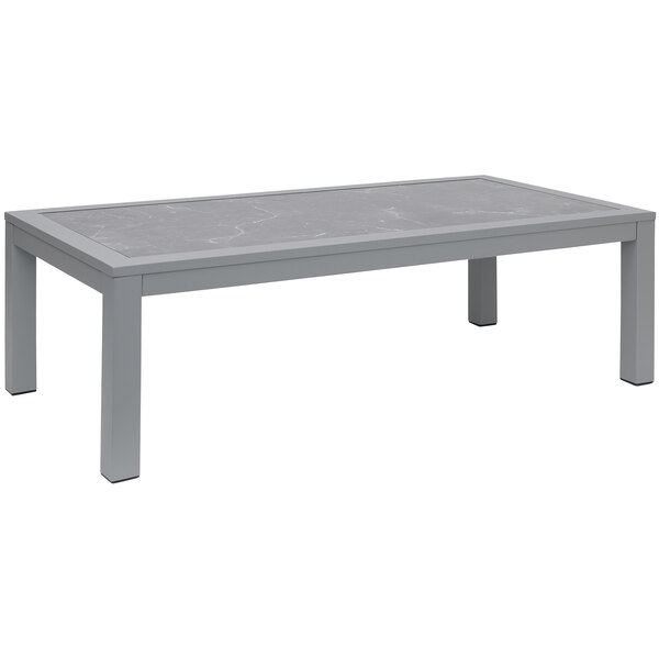 A BFM Seating Belmar soft gray aluminum rectangular table with a metal base and a glass top.