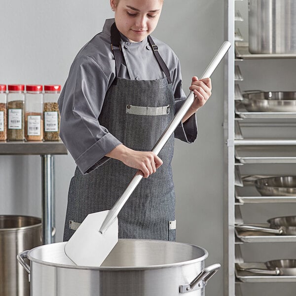 A woman in a chef's uniform using an American Metalcraft stainless steel paddle in a kitchen.