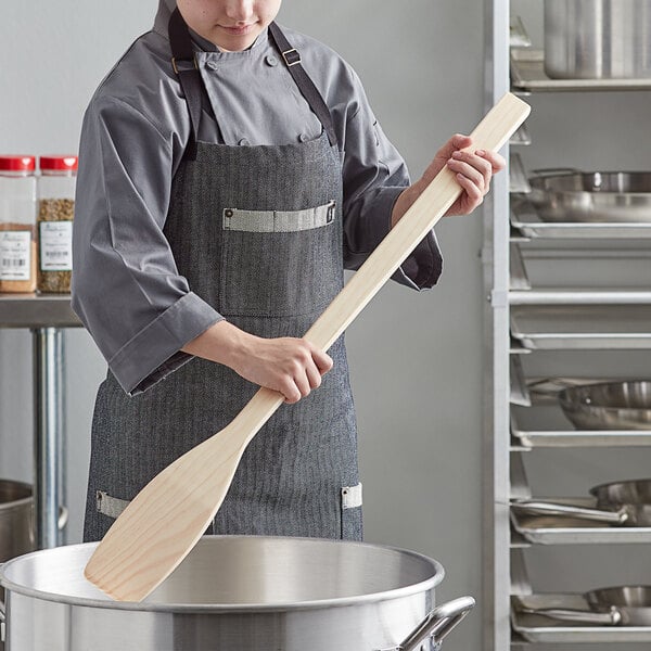A person in a professional kitchen using an American Metalcraft wood paddle.