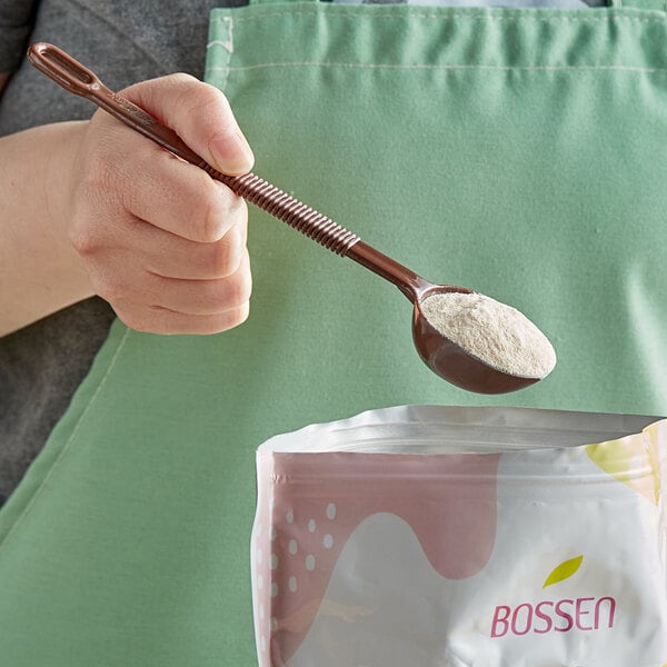 A hand holding a Bossen brown plastic measuring scoop over powder.
