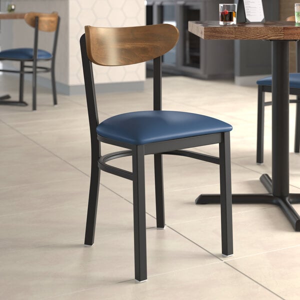A Lancaster Table & Seating Boomerang Series chair with a navy vinyl seat and vintage wood back at a table in a restaurant.