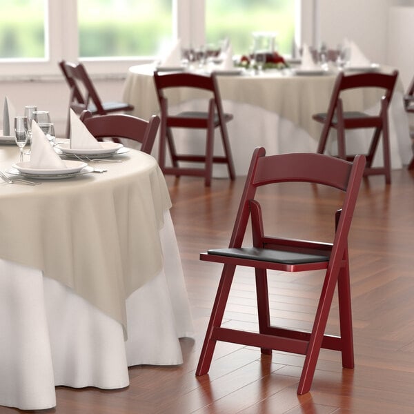 A Lancaster Table & Seating mahogany resin folding chair with a black cushion on a white background.