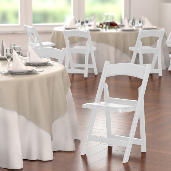 A white Lancaster Table & Seating folding chair with a white vinyl seat.