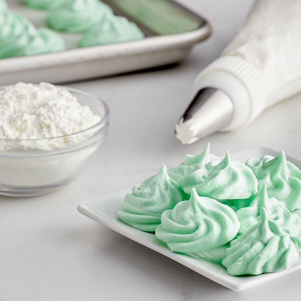 A white plate of green meringue next to a bowl of LorAnn Meringue Powder on a white surface.