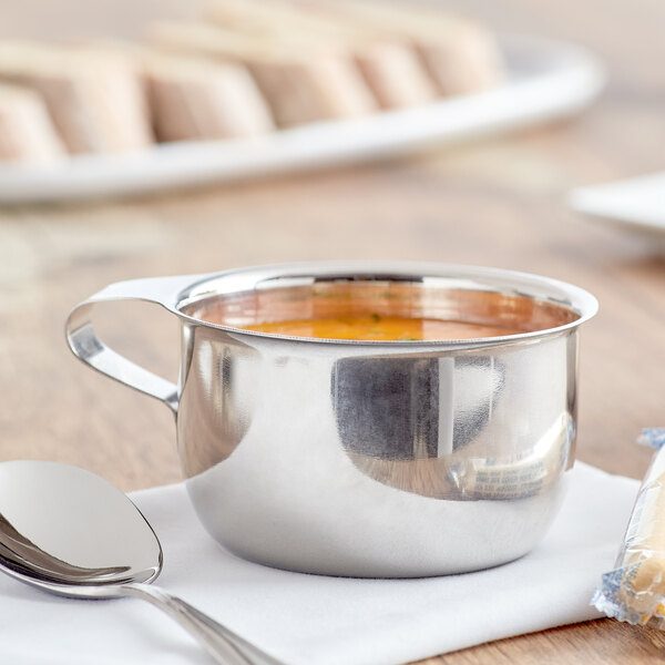 A Vollrath stainless steel round cup with soup and a spoon on a table.
