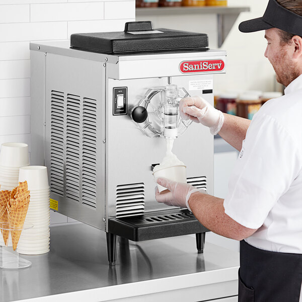 A man pouring ice cream into a SaniServ countertop soft serve ice cream machine.