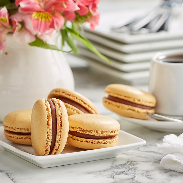 A white plate with three White Toque French caramel macarons and a cup of coffee on a table.