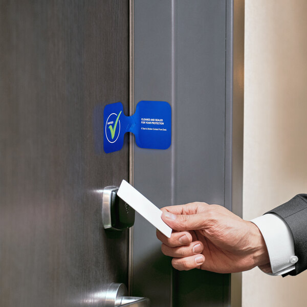A hand holding a white rectangular American Metalcraft blue "Sanitized" door seal card to a door.