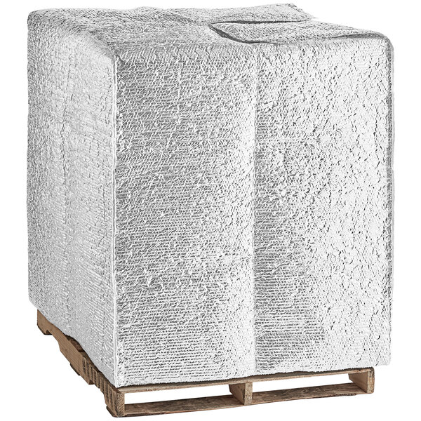 A white cube on a wooden pallet with a white blanket on top.