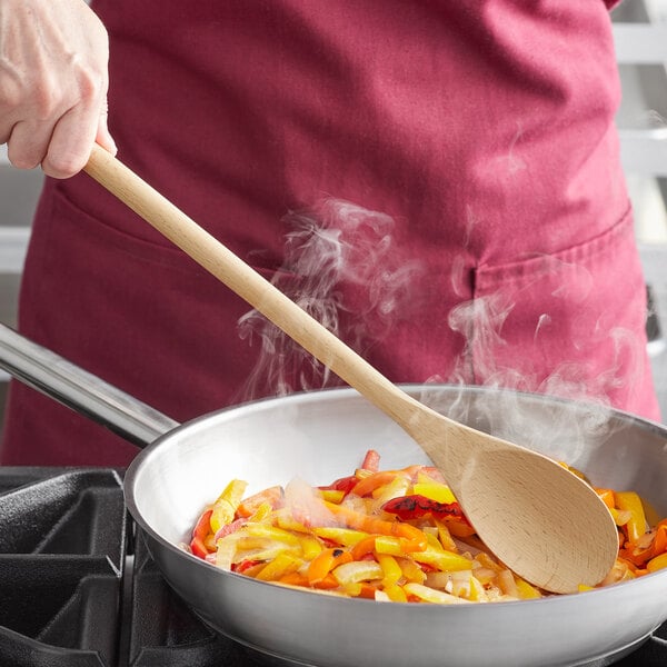 A person cooking food in a pan with a Tablecraft beechwood wooden spoon.