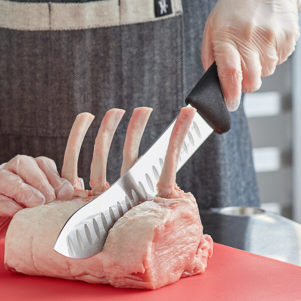 A person using a Mercer Culinary American Butcher Knife to cut meat on a red cutting board.