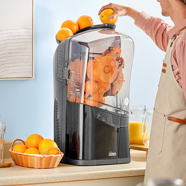 A man in an apron using a black Zumex juicer to make orange juice.