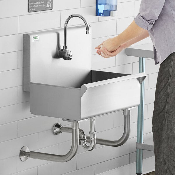 A person washing their hands in a Regency wall mounted hand sink.