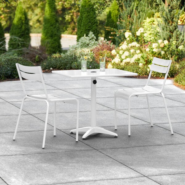 A white Lancaster Table & Seating outdoor table with two chairs on a stone patio.