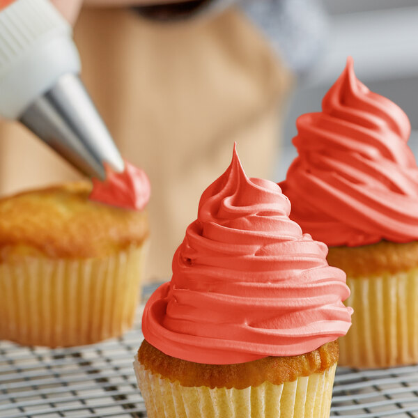 A person decorating a cupcake with Rich's Bettercreme Red Whipped Icing with a white tip.