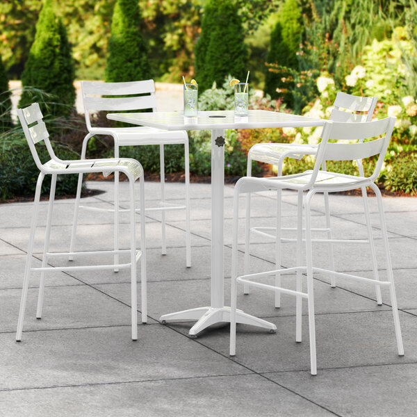 A Lancaster Table & Seating white bar height outdoor table with 4 white bar stools on a patio.