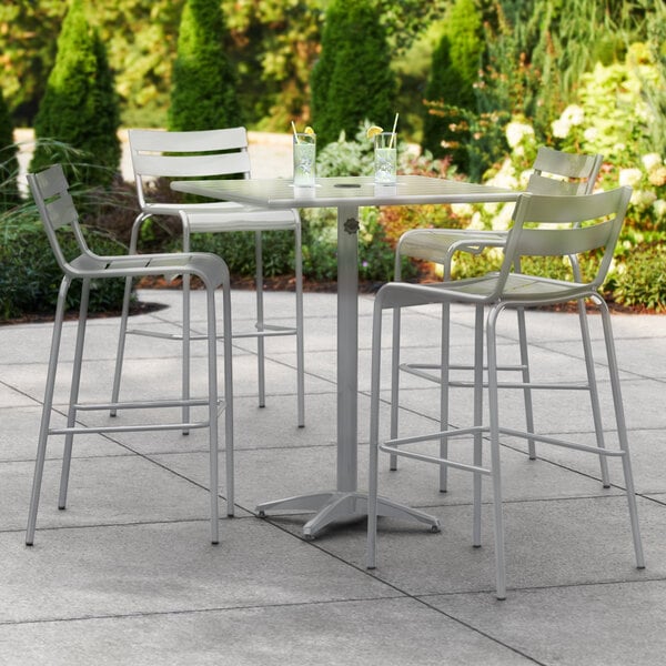 A Lancaster Table & Seating outdoor bar table with barstools on a patio.