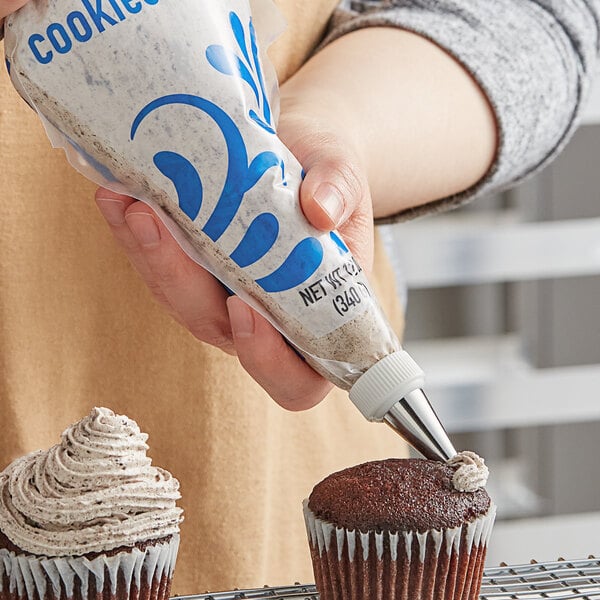 A person using Rich's Bettercreme Cookies 'N Creme Oreo Whipped Icing to frost a chocolate cupcake.