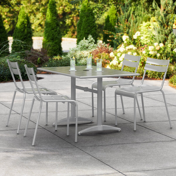 A Lancaster Table & Seating outdoor patio table and chairs with a white umbrella on a concrete patio.